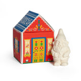 A small white gnome figurine next to a red house-shaped box with Nordic folk art patterns, containing bar soap labeled “Gnome’s Cottage.”.