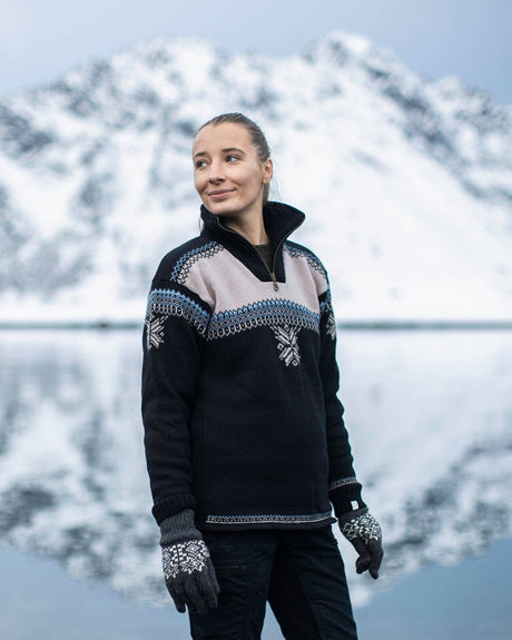 A woman wearing a Voss Women's Sweater (Black) stands outdoors in front of a snowy mountain and a body of water.
