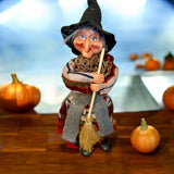 The Marketplace24 Kitchen Witch: Nonna Red 10" Tall with Broom stands on wood among pumpkins, bringing Scandinavian good luck charm to your Nordic kitchen decor. Her colorful dress and black hat pop against the blue background for a festive touch.