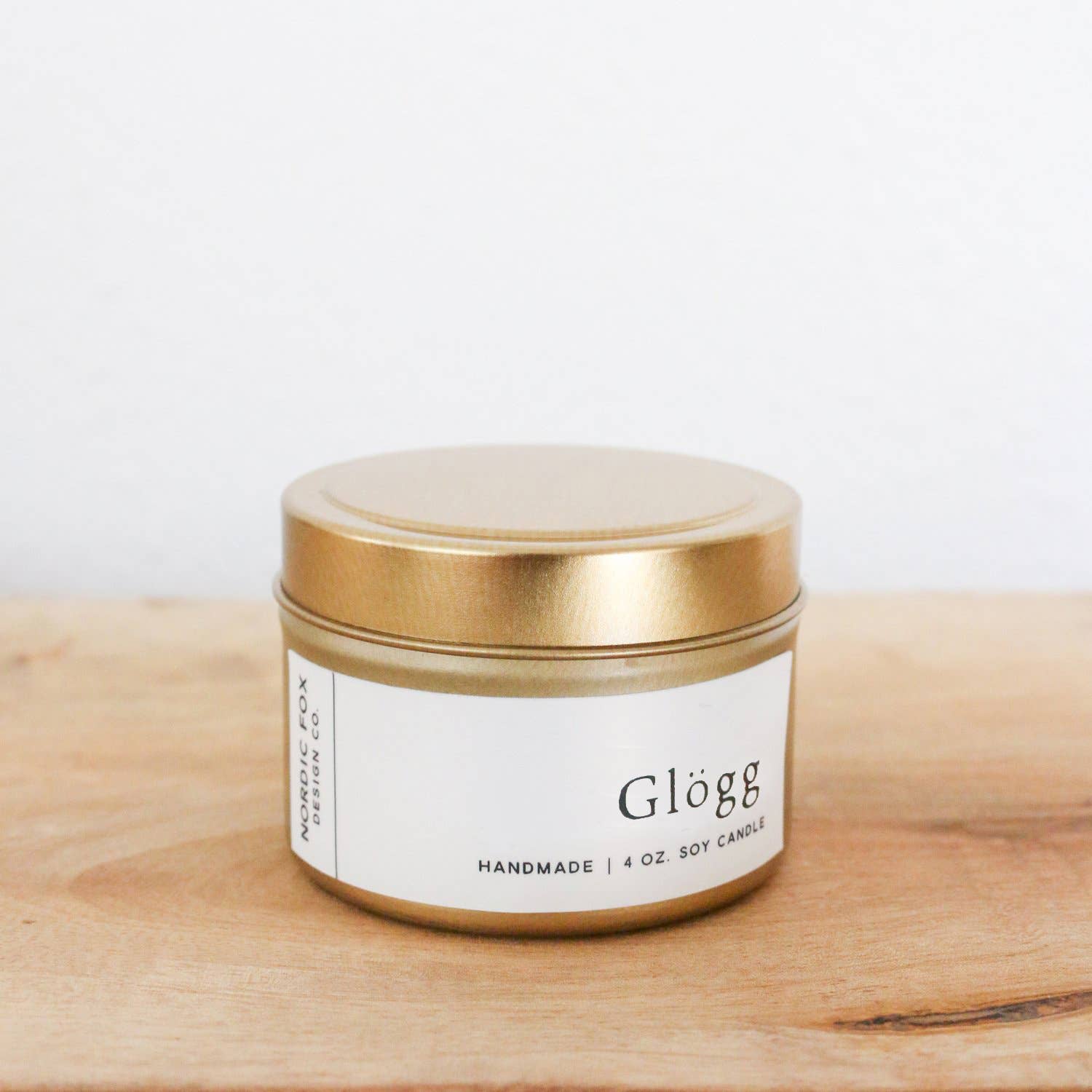 A 4 oz. tin of Candle: Glögg Handmade Soy Candle rests on a wooden surface against a white background, ready to fill your space with a cozy holiday scent.
