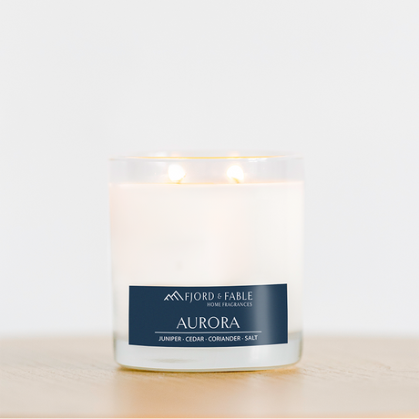 An Aurora Premium Soy Candle by Fjord & Fable, infused with essential oils and offering a fragrance blend of juniper, cedar wood, coriander, and salt, rests on a wooden surface.