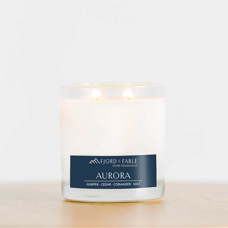 An Aurora Premium Soy Candle by Fjord & Fable, infused with essential oils and offering a fragrance blend of juniper, cedar wood, coriander, and salt, rests on a wooden surface.