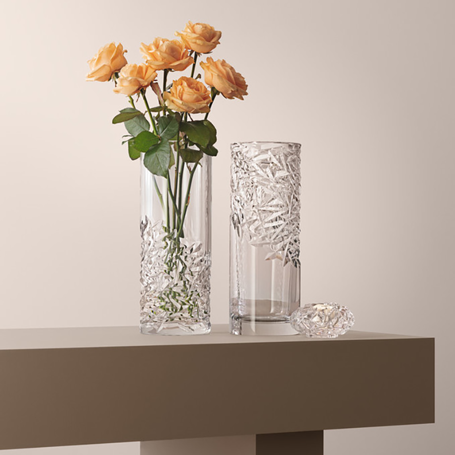 Three crystal pieces on a beige table: an Orrefors vase with orange roses, a clear empty vase, and a small faceted Carat Votive candle holder.