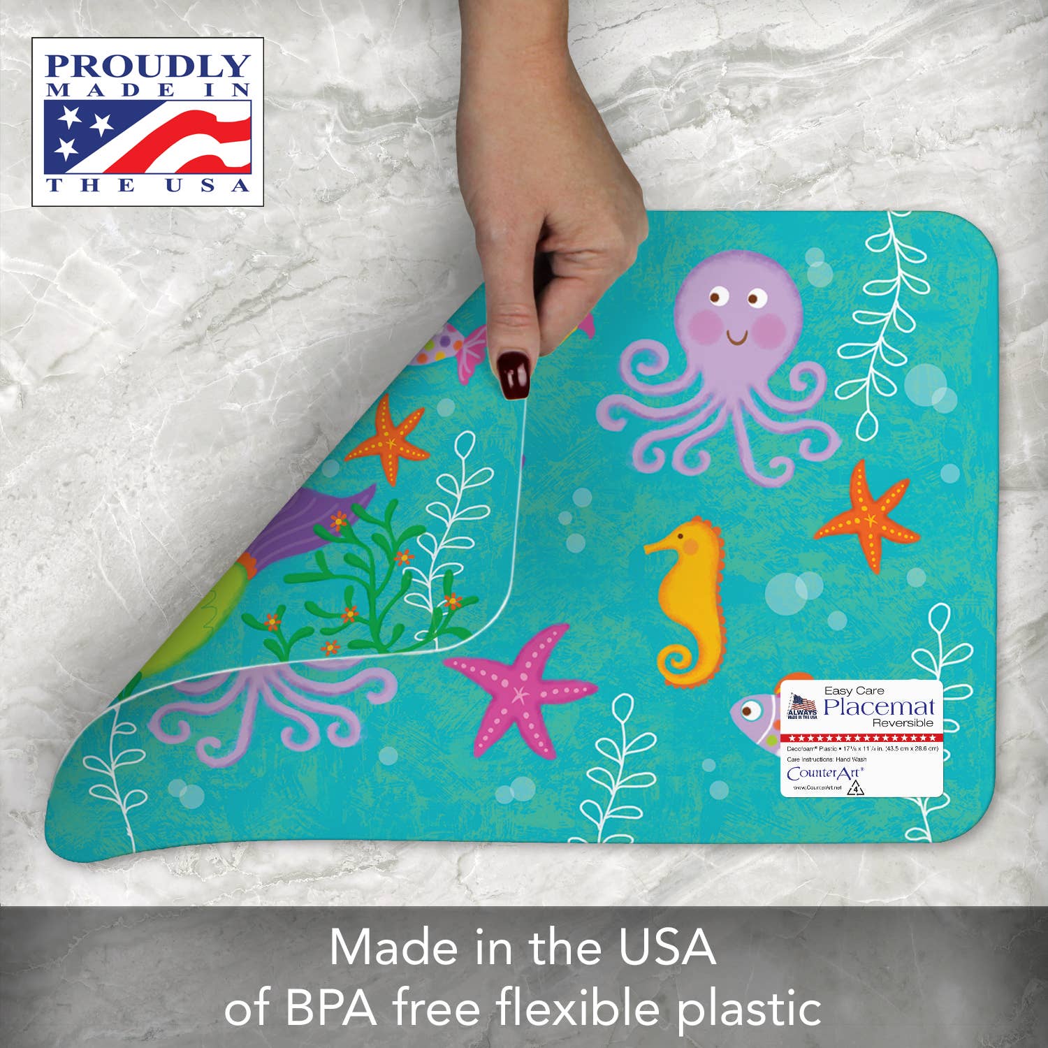 A hand lifts a corner of the Kids Mermaid Reversible Rectangular Plastic Placemat, which features sea creatures like an octopus and seahorse and proudly carries the label Made in the USA. These BPA-free placemats are easy to care for and make an ideal housewarming gift with their flexible plastic design.