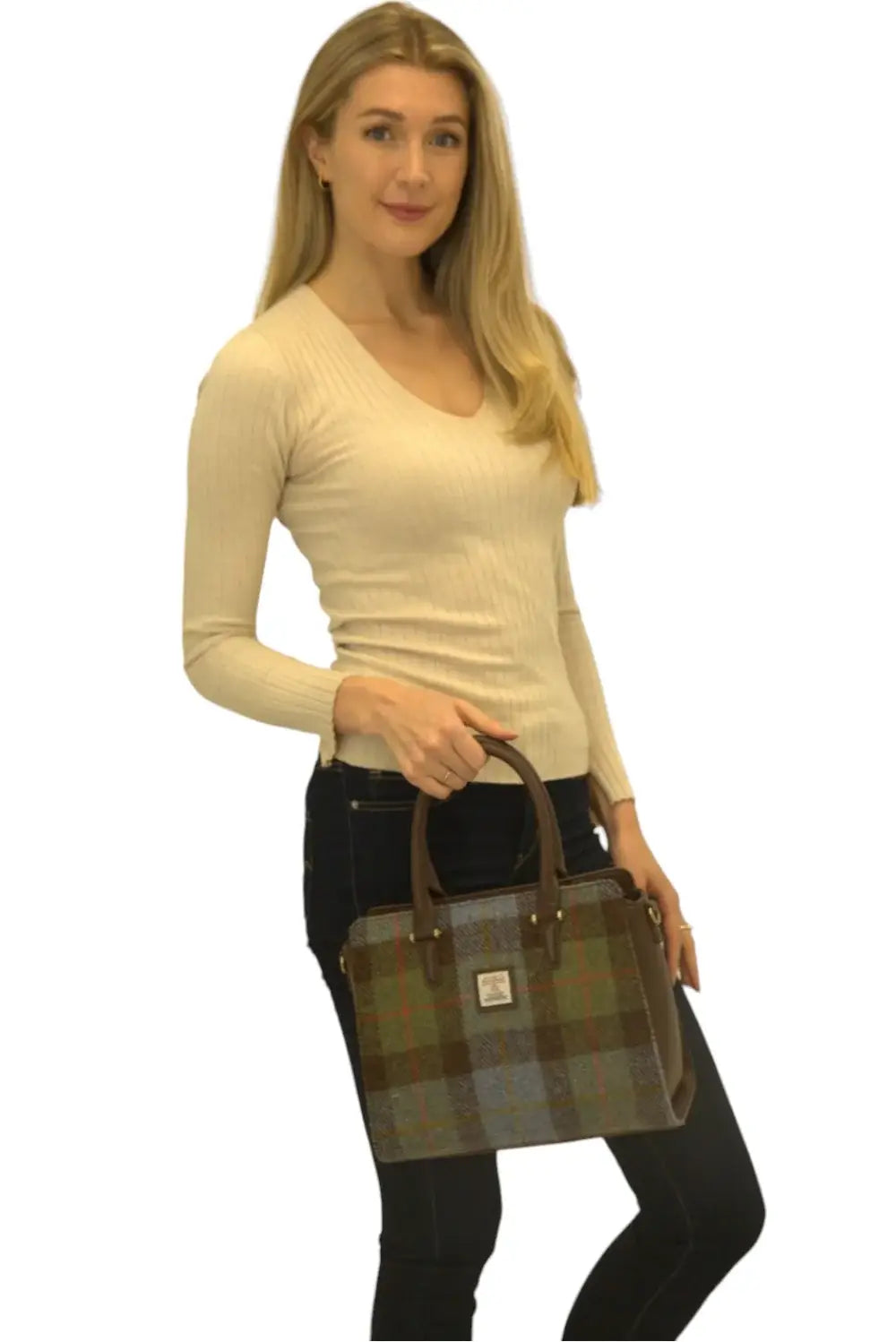 A woman holds the Harris Tweed Double Handle Tote in dark brown, wearing a beige long-sleeve top and dark jeans, against a plain white background.
