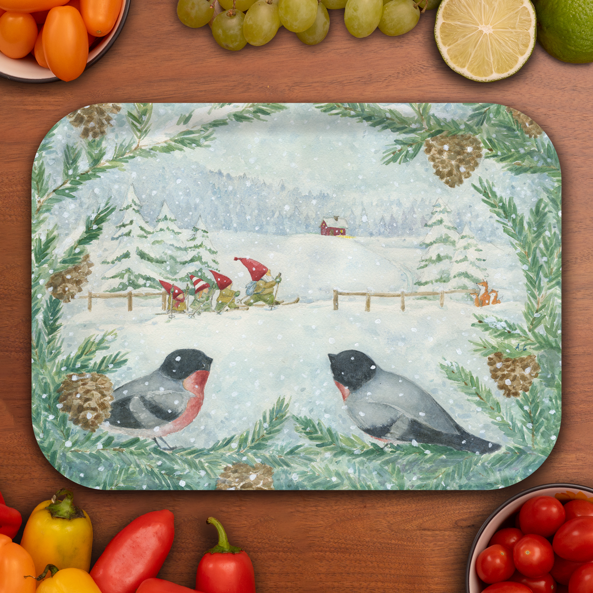 Birchwood tray with a snowy winter scene featuring two birds, pine cones, gnomes skiing by trees and a red house, surrounded by assorted fruits and vegetables.