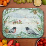 Birchwood tray with a snowy winter scene featuring two birds, pine cones, gnomes skiing by trees and a red house, surrounded by assorted fruits and vegetables.