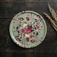 Round serving tray featuring a pink and purple floral design on Nordic birch veneer, placed on a dark wooden surface next to dried wheat stalks.