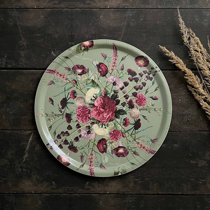 Round serving tray featuring a pink and purple floral design on Nordic birch veneer, placed on a dark wooden surface next to dried wheat stalks.