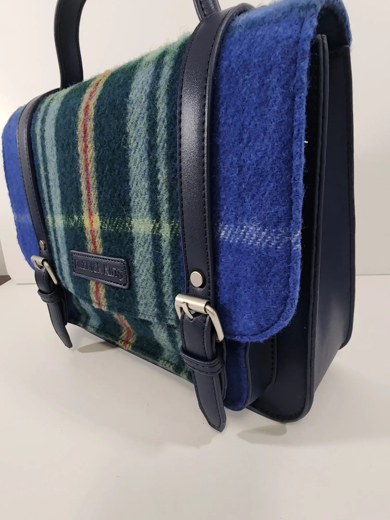 The Nova Scotia Patsy Handbag features blue, green, and red provincial tartan wool with navy leather straps and edges, displayed on a white surface.