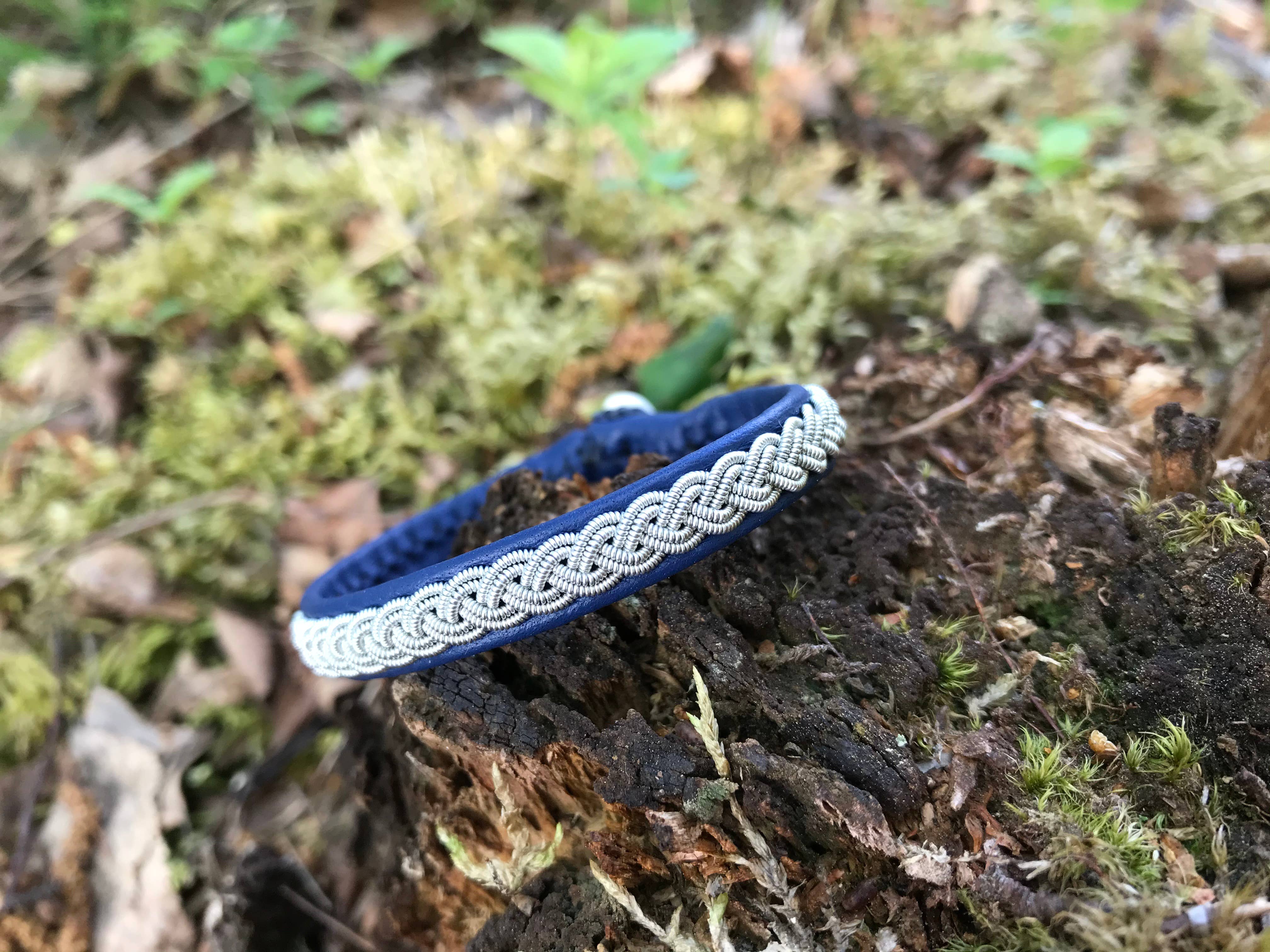 The Bracelet: Lapland Sami Tin Bracelet Single Braid #1: Blue Gray, inspired by handmade Lapland jewelry, is shown on a mossy tree stump in an outdoor setting.