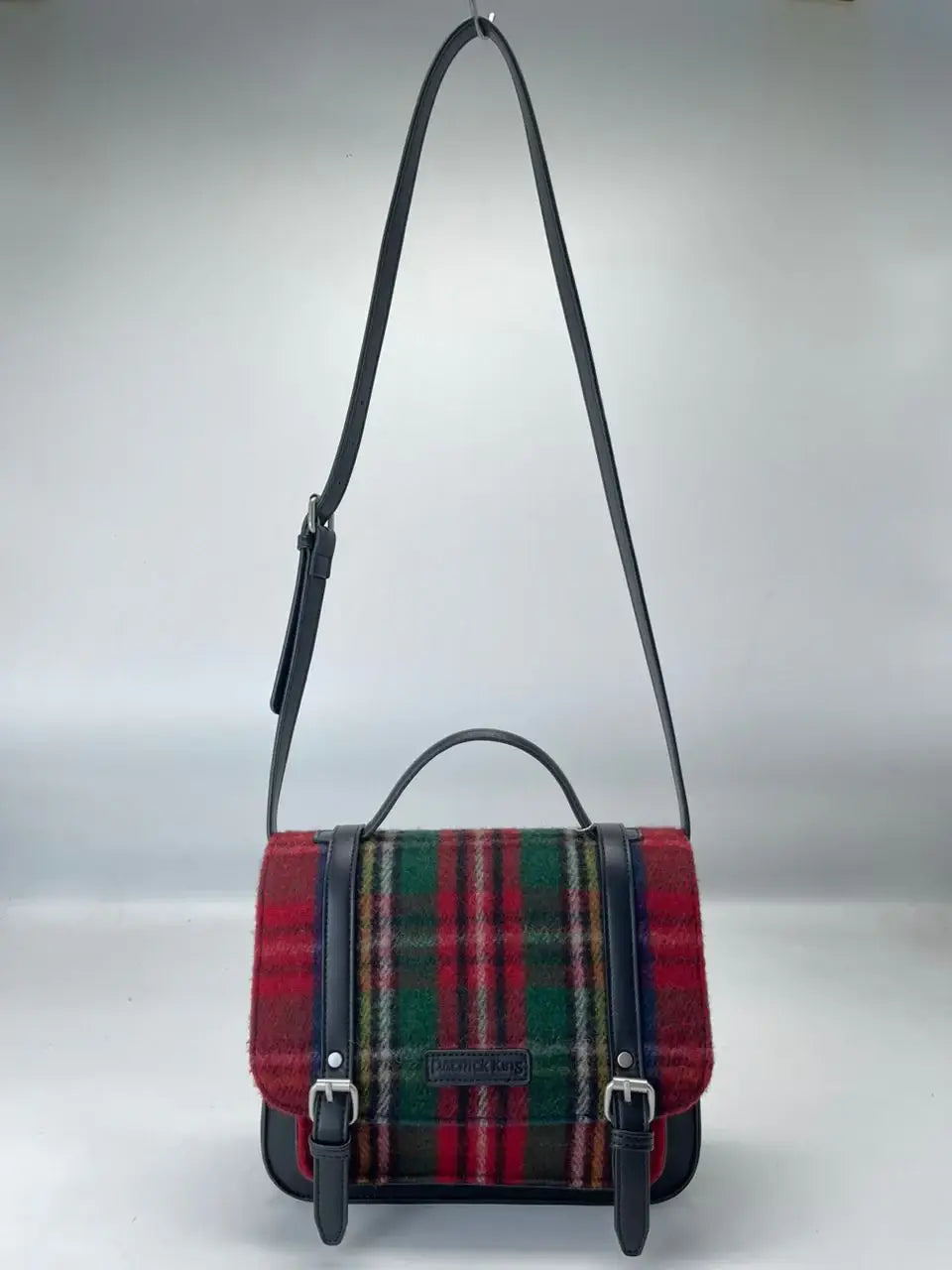 The Bag: Royal Stewart Handbag showcases a red, green, and yellow Scottish tartan plaid fabric flap, black leather trim, top handle, and adjustable shoulder strap, displayed against a plain background.