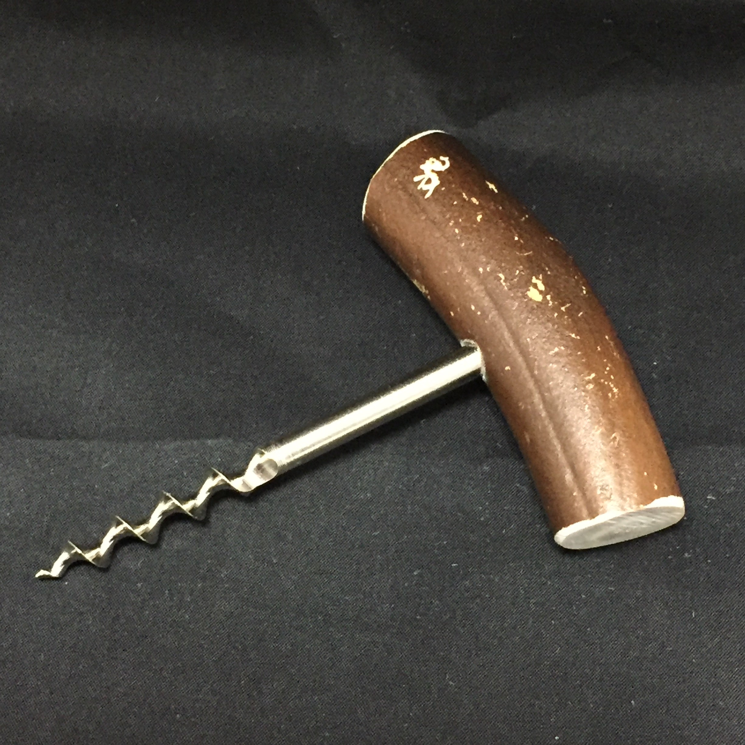 The Reindeer Antler corkscrew, featuring an elegantly carved wooden handle, rests on a black fabric surface.