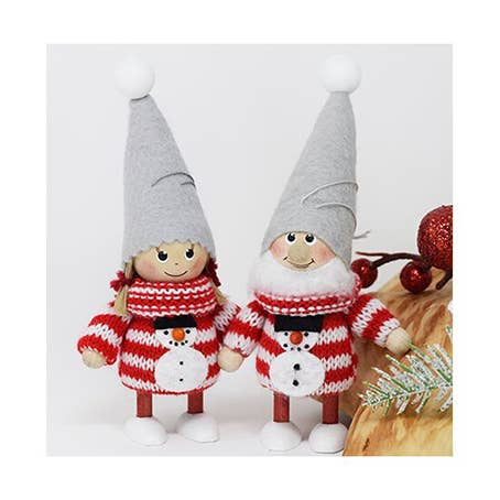 Two festive, handmade gnome figurines featuring gray hats and red-and-white striped snowman sweaters elegantly stand on a wooden surface adorned with berries and pine sprigs, infusing Scandinavian charm into your Christmas tree display with the "Ornament: Girl in red sweater with snowman.