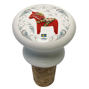 Wine bottle stopper with cork base and round white top, decorated with a red Swedish Dala Horse, Swedish flag, and blue floral patterns.