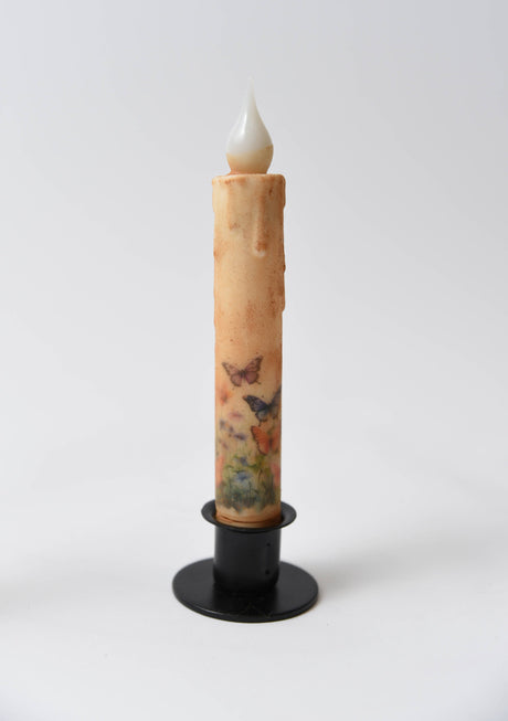 The Butterfly Panorama LED Timer Taper Candle: Top Dusted features a battery-operated design with butterfly and flower motifs, displayed in a black holder on a white background.