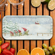 Birchwood tray featuring gnomes in red hats skiing through snow by pine trees, with a red house on a snowy hill. Surrounded by glasses and assorted fruits.