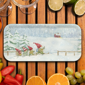 Birchwood tray featuring gnomes in red hats skiing through snow by pine trees, with a red house on a snowy hill. Surrounded by glasses and assorted fruits.