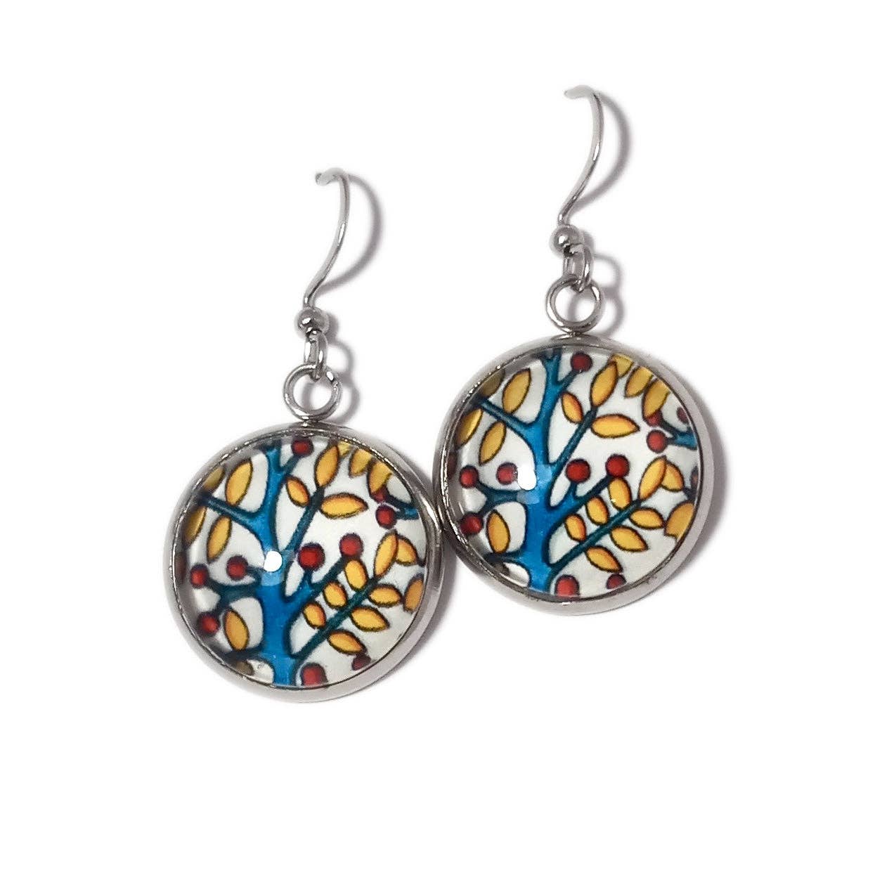 These Sarah Angst Art earrings, named 'Branches,' are round and handmade, showcasing a tree design with yellow and red leaves on a blue and white background. They are set in silver-toned metal and feature hooks for easy wearing.