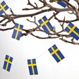 A bare tree branch displays two 6-foot Swedish Flag Garlands, adding a Scandinavian touch with the Ornament: Swedish Flag Garland (2) to a plain background.