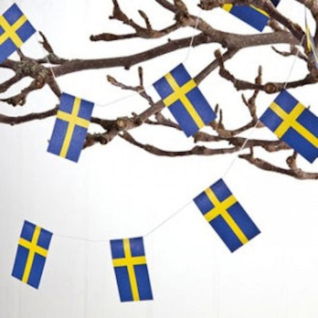 A bare tree branch displays two 6-foot Swedish Flag Garlands, adding a Scandinavian touch with the Ornament: Swedish Flag Garland (2) to a plain background.