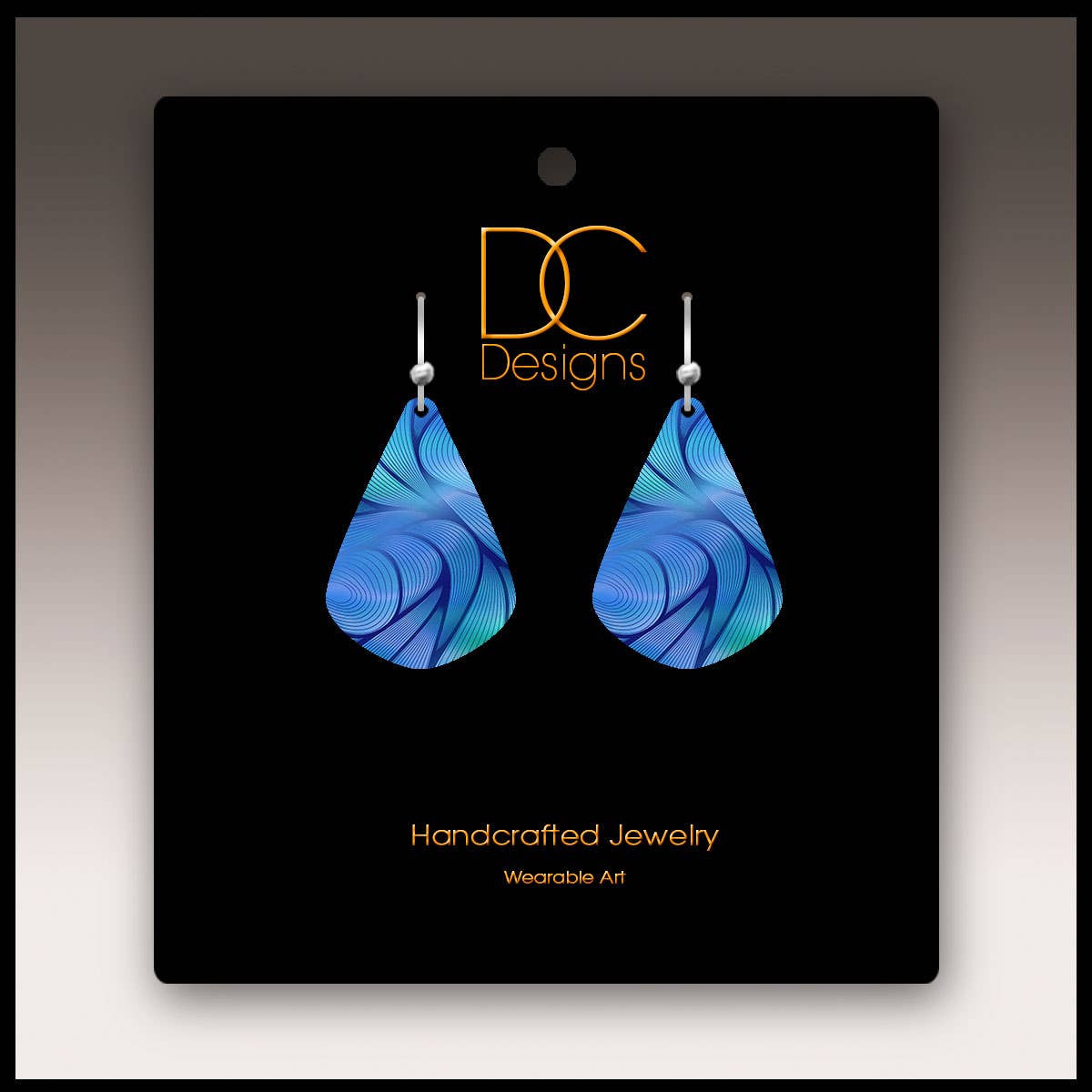 The Midnight Aurora Abstract Short Drop Handmade Earrings are blue, teardrop-shaped with swirling patterns, shown on a black DC Designs “Handcrafted Jewelry Wearable Art” card. Made with hypoallergenic stainless steel for comfort.