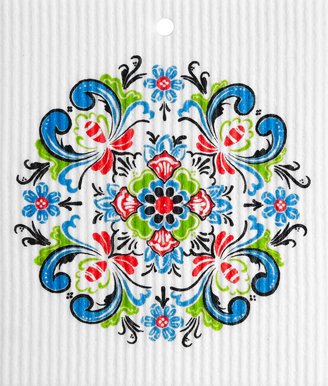 The Dish Cloth: Rosemaling Norwegian Design features a symmetrical floral pattern in red, blue, green, and black on a white textured background, with a small hole near the top center.