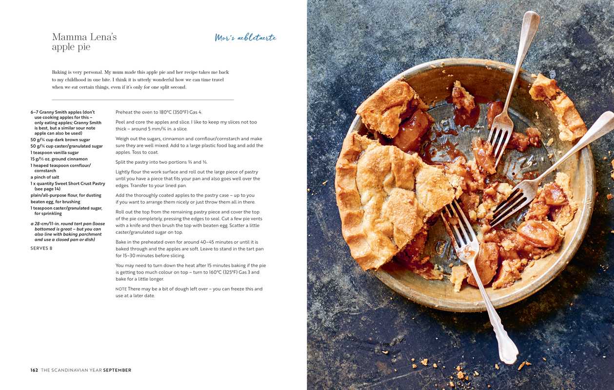 A copy of "Scandinavian Year" by Bronte Aurell lies on a blue surface next to a partially eaten apple pie, its filling exposed where a slice is missing, while the pie dish and serving knife rest among scattered crumbs.