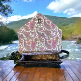 A Grey Harris Tweed Large Satchel sits with its flap open on a wooden surface outdoors, surrounded by a river and green hills in the background.