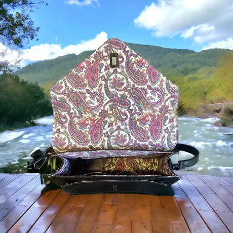 A Grey Harris Tweed Large Satchel sits with its flap open on a wooden surface outdoors, surrounded by a river and green hills in the background.