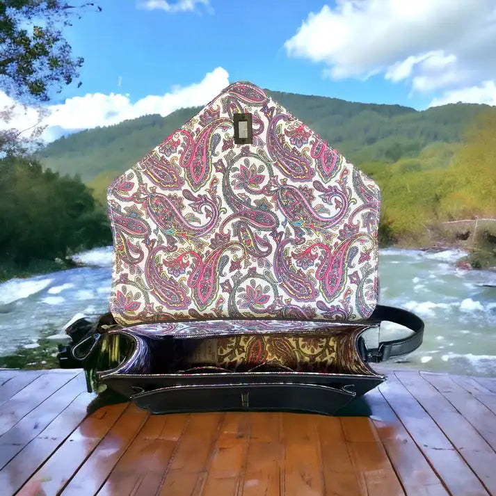A Grey Harris Tweed Large Satchel sits with its flap open on a wooden surface outdoors, surrounded by a river and green hills in the background.