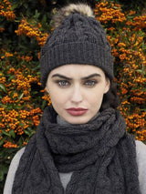 A woman with dark hair wears the Chunky Cable Hat - Charcoal (One Size) as she stands in front of a bush with orange berries.