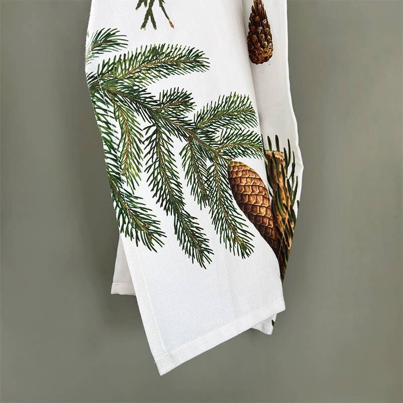 A Pine trees tea towel, crafted entirely from 100% organic cotton by Koustrupco, features elegant green pine branches and brown pinecone designs against a light green backdrop.