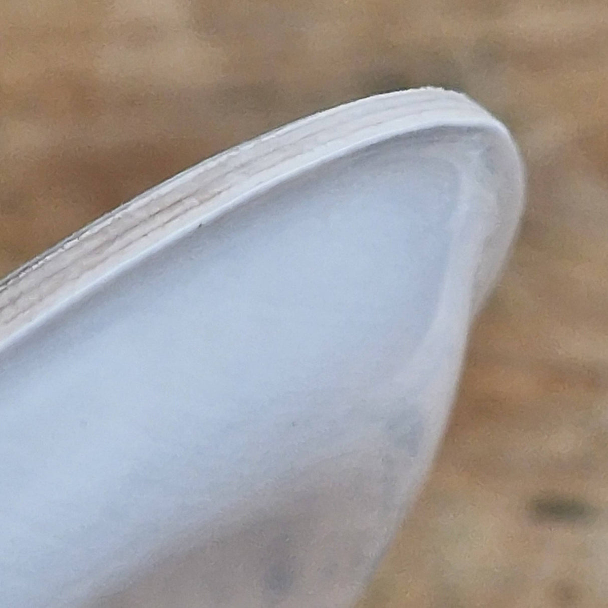 Close-up of a white high-heeled shoe's pointed toe resting on the Swedish Dala Horse Birchwood Coaster by Lotta Spjute Sweden, with a blurred brown background.