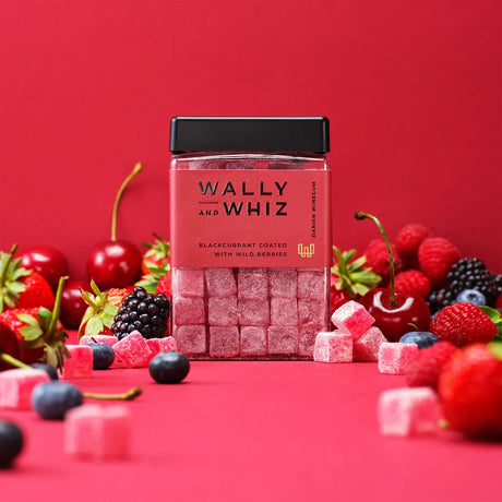 A jar of Wally & Whiz Blackcurrant with Strawberry gummy candy is surrounded by assorted berries: strawberries, cherries, blackberries, blueberries, and raspberries against a red background. Enjoy these vegan and gluten-free Danish sweets (240g).