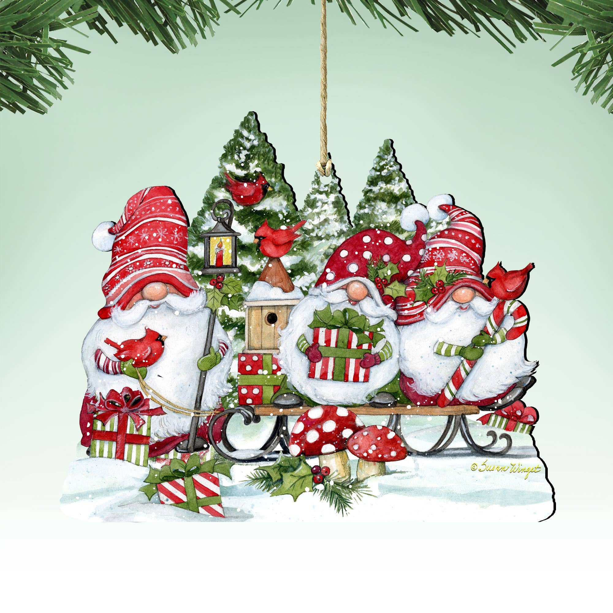 The Christmas Gnomes Ornament by Susan Winget (5" x 5.5" x 0.25") features three red-hatted gnomes on a sleigh with gifts, birdhouses, cardinals, and snowy trees—a charming handcrafted addition to your holiday décor.
