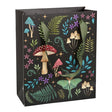 The Gift Bag: Dark Forest Mushroom Bag (7.5"w x 9"h x 3.5"d) features a mystical design of flora and fauna with illustrations of mushrooms, ferns, and flowers set against a black background, complemented by green handles.