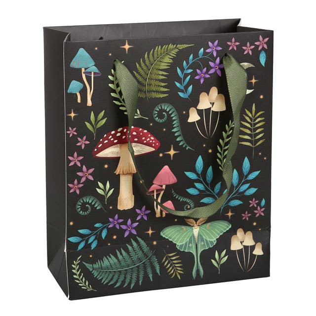 The Dark Forest Gift Bag, measuring 7.5 inches in width by 9 inches in height and 3.5 inches in depth, features mystical flora and fauna on its print, with green handles accentuating vibrant mushrooms, ferns, flowers, and a moth against a black background.