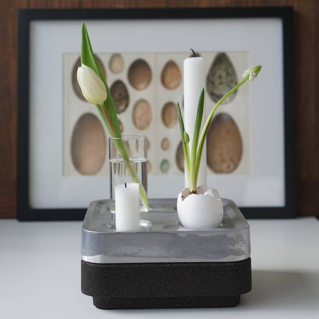 The Candle Holder: Mini Vases for Stumpastaken Candleholder 2-pack features white tulips and plants in eggshells, arranged with a candle on layered surfaces and framed egg art, making a charming table decoration.