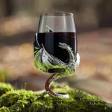 The Wine Glass: Medieval Dragon Viking Goblet Mug (9oz) features a fantasy-inspired silver dragon stem and base, filled with red wine and resting on moss outdoors—an enchanting medieval drinkware piece.