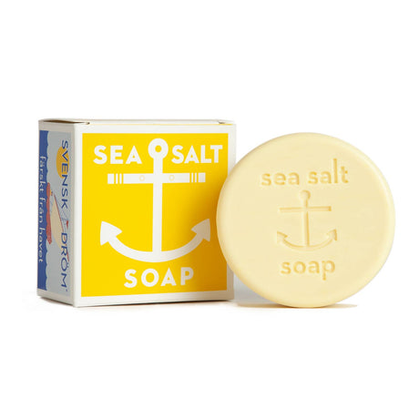 Soap: Sea Salt Lemon Soap Swedish Dream, a round exfoliating bar with anchor design and embossed text, shown beside its yellow and white box featuring an anchor illustration and "Sea Salt Soap." Made with all-natural ingredients.