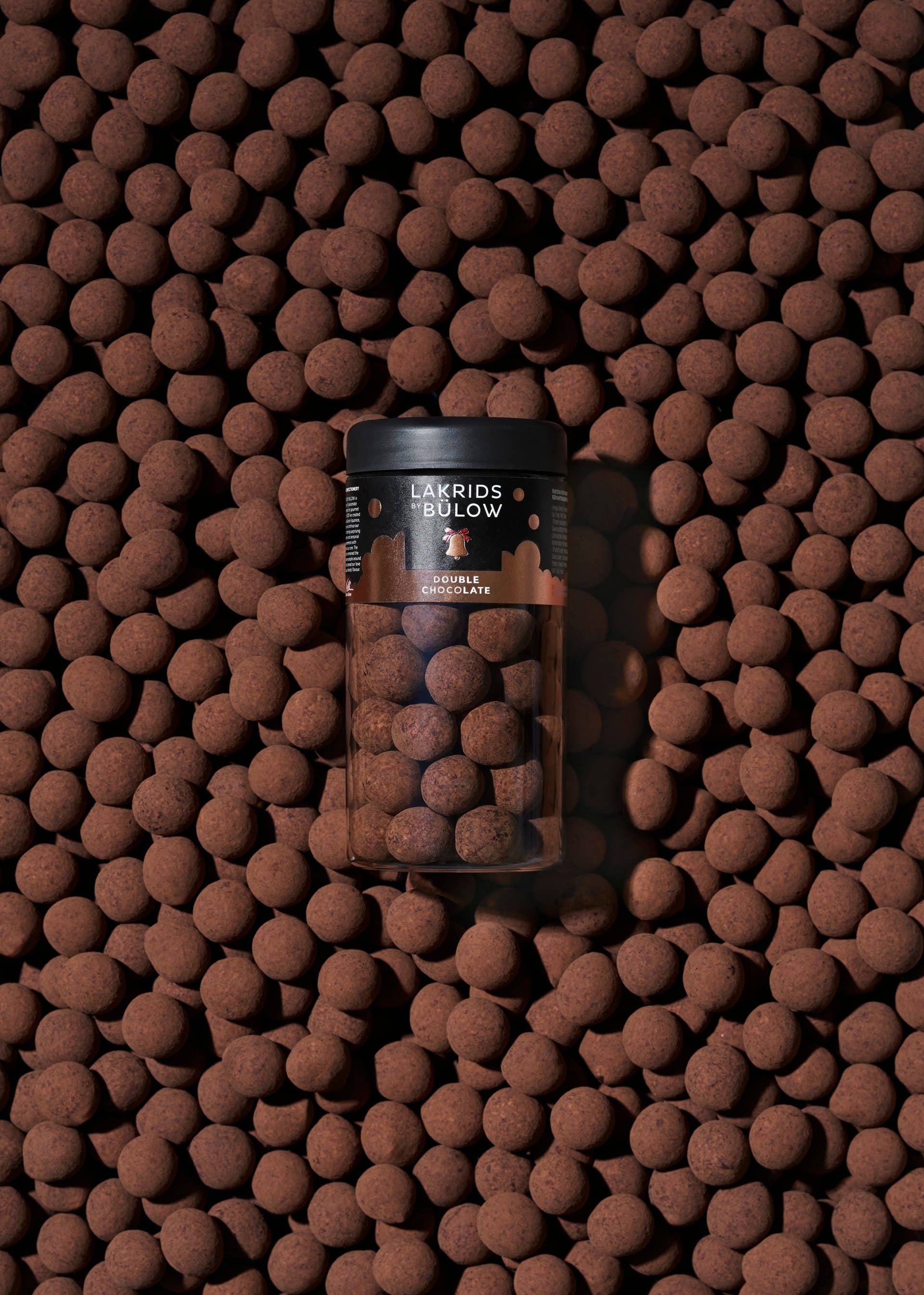 A clear jar of Candy: Double Chocolate – Danish Gourmet Licorice (Small, Limited Edition) stands upright, surrounded by matching chocolate-coated licorice pieces, highlighting this limited-edition Danish treat.