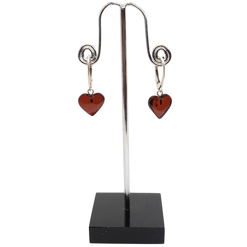 Heart Cherry Amber Sterling Silver Earrings with red heart-shaped pendants, reminiscent of cherry amber, are displayed on a black upright stand.