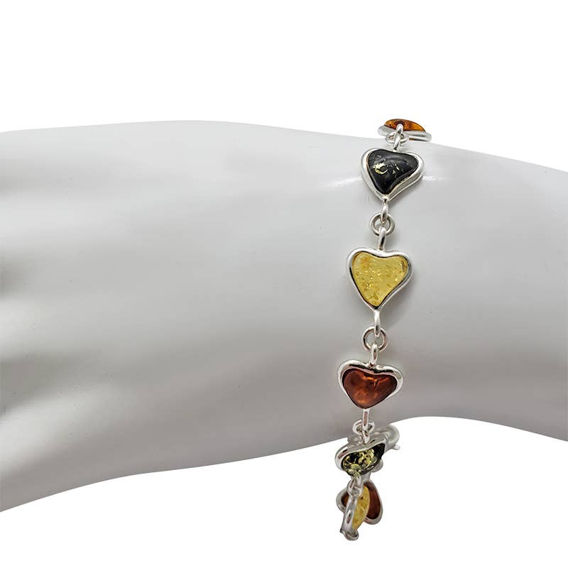 The Multi-Color Amber Sterling Silver Heart Bracelet, elegantly displayed on a mannequin hand, features genuine Baltic amber charms in black, yellow, and amber hues.