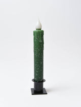 The Diamond Dusted Christmas LED Timer Taper Candle is a tall, green battery-operated candle with a white flame-like tip and small white speckles, set in a black holder against a plain white background.
