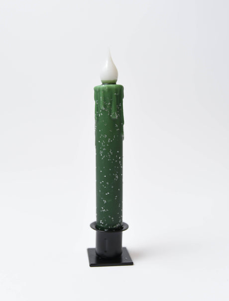 The Diamond Dusted Christmas LED Timer Taper Candle is a tall, green battery-operated candle with a white flame-like tip and small white speckles, set in a black holder against a plain white background.