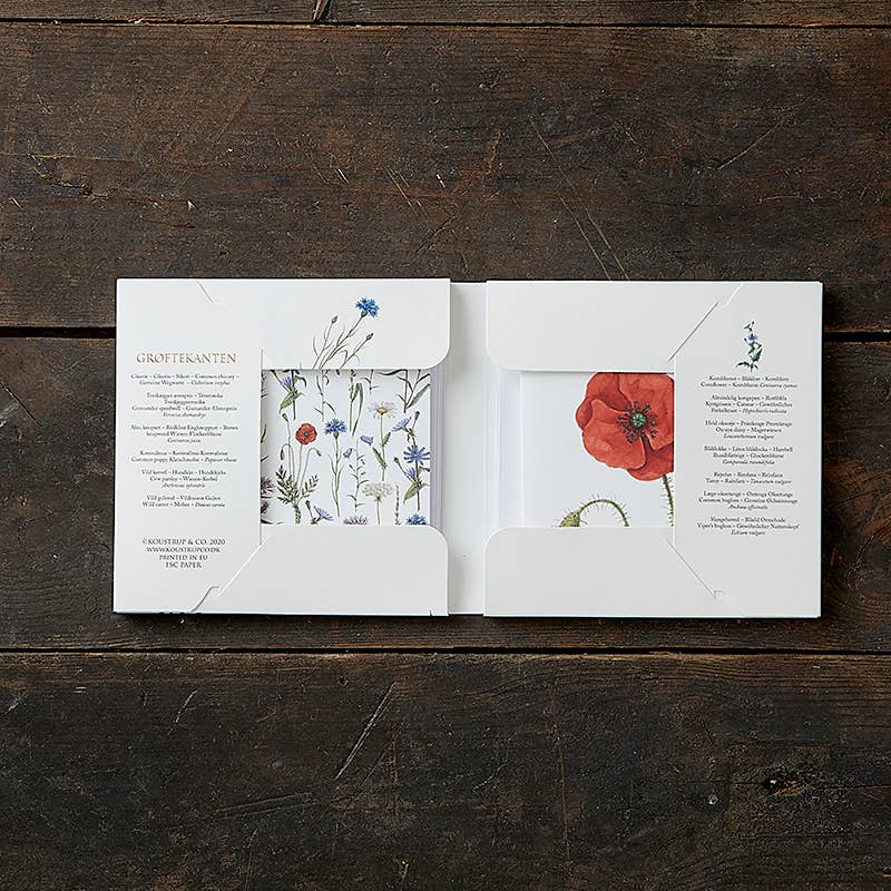 The Card Pack: Hedgerow Square, featuring a floral-themed card folder with a fold-out design, is open on a wooden surface, displaying illustrations of wildflowers and text on each panel. This eco-friendly choice for any event comes paired with FSC certified envelopes.