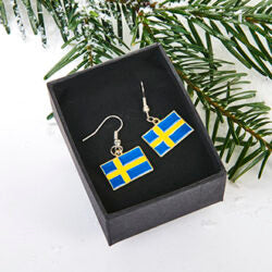 Earrings: Swedish Flag Earrings 3/4 x 1/2 Flags are presented in a black box, accented by pine branches and snow for a festive, international touch.