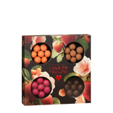 Showcasing the Candy: Gift Box LOVE 2026—a square selection box from Lakrids by Bülow Denmark—this arrangement features four round windows displaying assorted colored chocolate-coated licorice balls. The gluten-free LOVE box stands out against a vibrant floral and strawberry-patterned background, offering an enticing selection of confections.