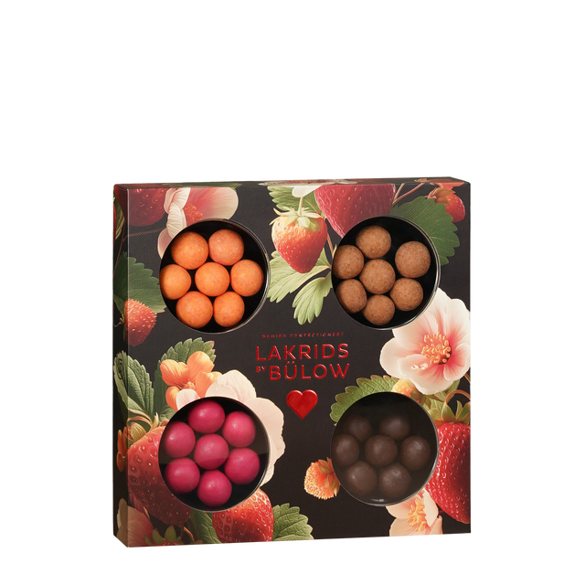 Showcasing the Candy: Gift Box LOVE 2026—a square selection box from Lakrids by Bülow Denmark—this arrangement features four round windows displaying assorted colored chocolate-coated licorice balls. The gluten-free LOVE box stands out against a vibrant floral and strawberry-patterned background, offering an enticing selection of confections.